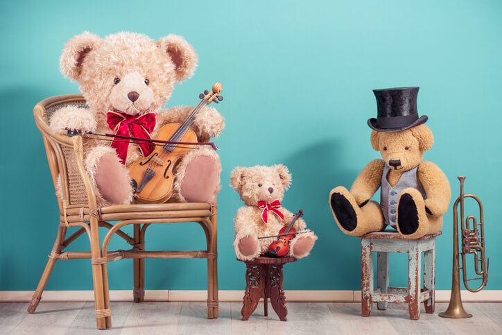 Three retro Teddy Bear toys with fiddles, cylinder hat sitting on wooden chairs, brass trumpet front aquamarine wall background
