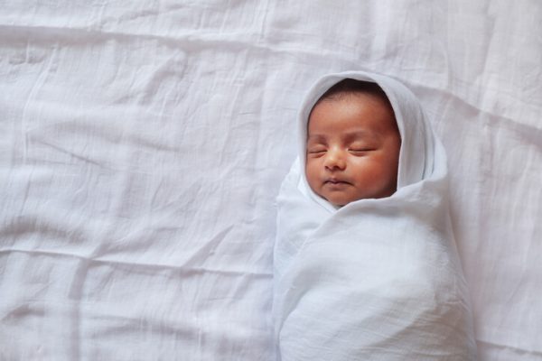 A one month old baby sleeping and swaddled in white cloth lying in white cloth