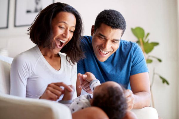 Happy mixed race young adult parents playing with their three month old baby son