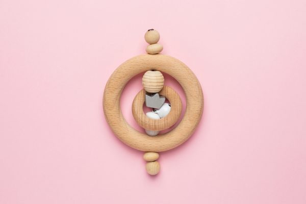 Wooden baby toy rattle on pink background, natural eco materials