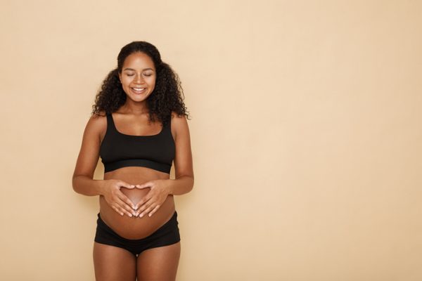 Pregnant woman holding hands on her belly making a heart symbol