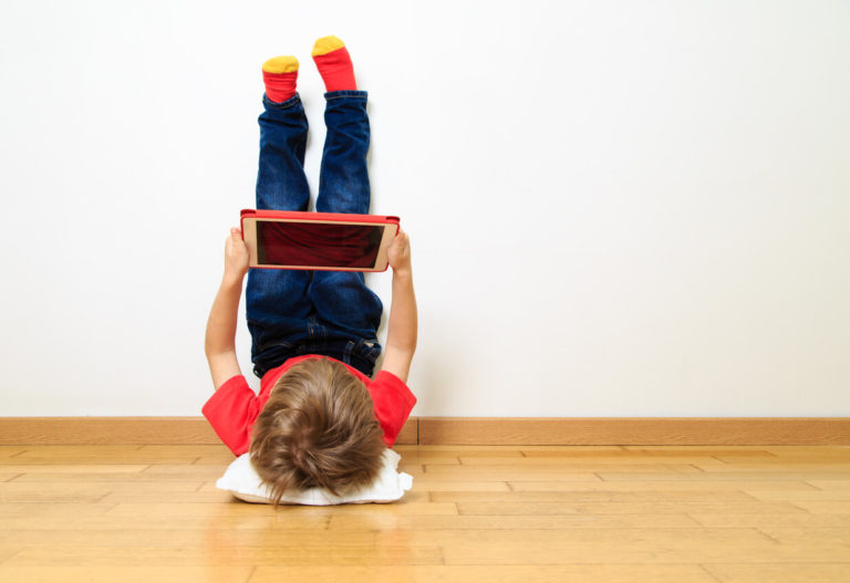 Little boy resting his feet on the wall looking at a tablet