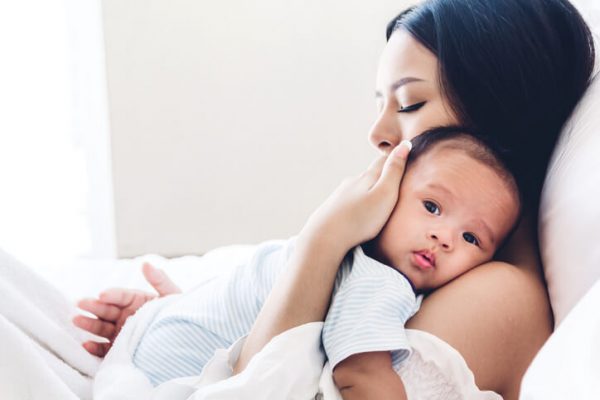 Mother holding baby in her arms and kiss in a white bedroom