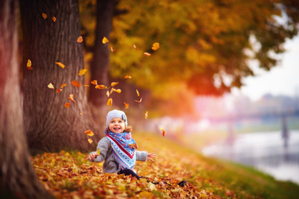 Adorable happy baby girl throwing the fallen leaves up, playing in the autumn