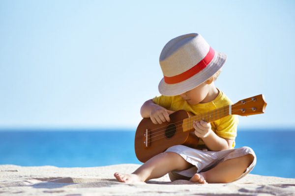 young baby boy sitting on a beach with a guitar