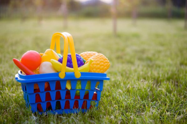 Bright plastic colorful basket with toy fruits and vegetables outdoors on sunny summer day
