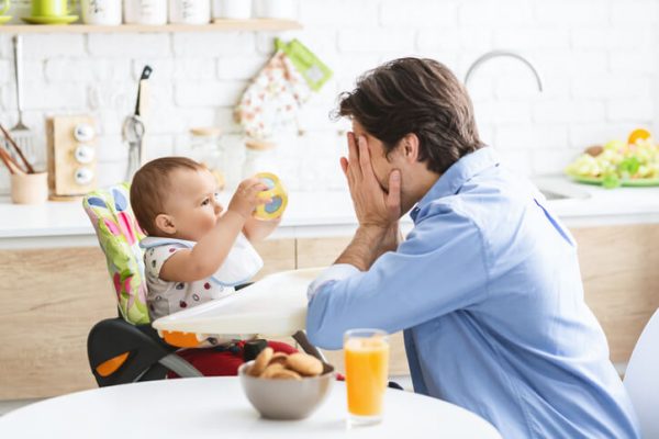 Cheerful daddy playing with cute baby son in kitchen