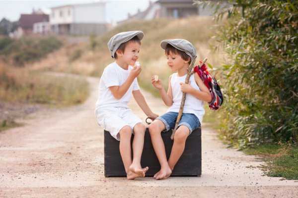 Two boys, sitting on a big old vintage suitcase, eating