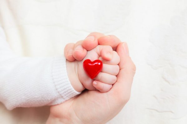 Hands of mother and baby closeup holding heart
