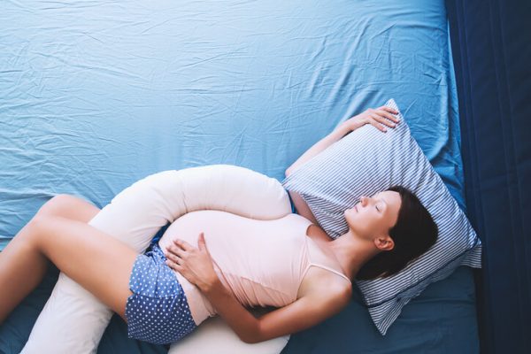 Beautiful pregnant woman relaxing or sleeping with tummy supporting pillow at bed