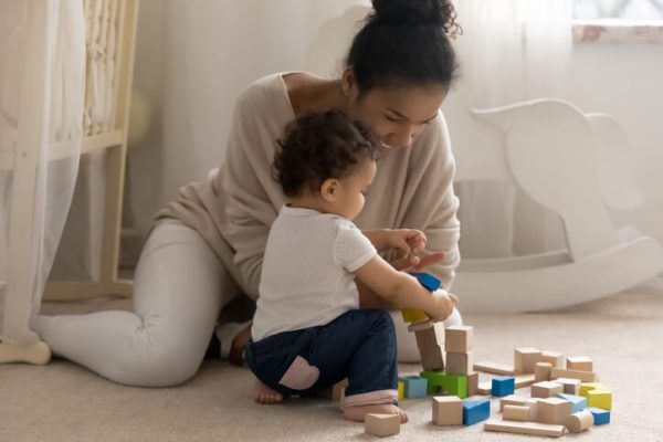 Affectionate african mother constructing building with cubes with small kid