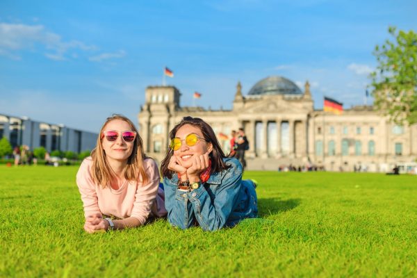 Two Young happy girls wearing sun glasses lying on a grass and have fun in front of the Bundestag building in Berlin