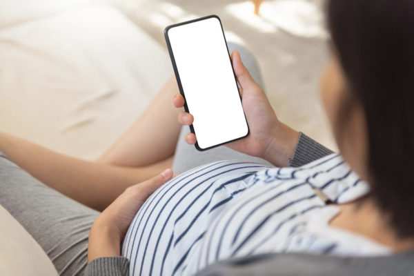 sian Pregnant woman using smartphone and doing online shopping on sofa