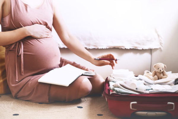 Pregnant woman packing bag for maternity hospital, making notes, checking list in diary
